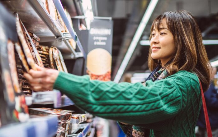 Mujer joven comprando comida preparada frente a un refrigerador en el supermercado.